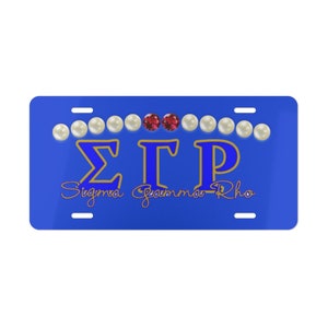 May include: Blue license plate with the letters "ΣΓΡ" in gold and blue, with the words "Sigma Gamma Rho" in cursive below. The letters are surrounded by a row of white pearls and two red gems.