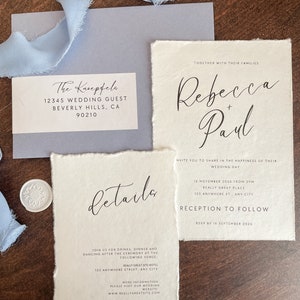 May include: Wedding invitation with a cream background and black text. The invitation reads "Rebecca + Paul" and includes the wedding date, time, and location. The invitation also includes details about the reception to follow.