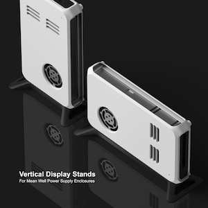 May include: Two white plastic vertical display stands for Mean Well power supply enclosures. Each stand features a circular fan cutout and three horizontal ventilation slots on the side. The text "Vertical Display Stands For Mean Well Power Supply Enclosures" is printed in white at the bottom left.
