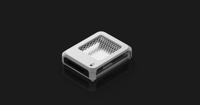 Op de afbeelding: Een wit rechthoekig elektronisch apparaat met een honingraatgaas bovenkant en een kleine knop. Het apparaat heeft een strak, modern ontwerp en staat tegen een donkere achtergrond. Het apparaat lijkt een computercomponent te zijn.