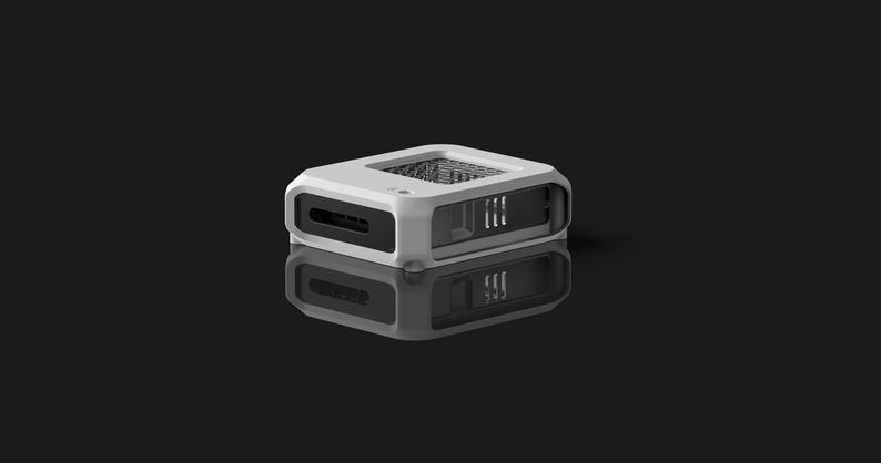 Peut inclure: Un appareil rectangulaire blanc et noir avec un dessus en maille et une fente sur le c&ocirc;t&eacute;. L'appareil se refl&egrave;te sur une surface sombre. Le design est moderne et minimaliste.