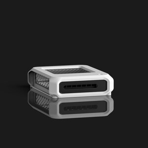 Op de afbeelding: Een wit en zwart rechthoekig elektronisch apparaat met een mesh-bovenkant en een reeks sleuven aan de voorkant. Het apparaat wordt weerspiegeld op een zwart oppervlak. Het apparaat lijkt een kleine computercomponent te zijn.