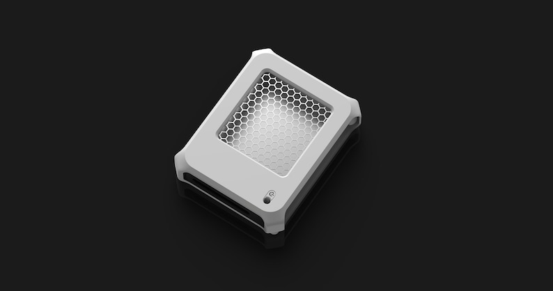 Op de afbeelding: Een wit en grijs rechthoekig apparaat met een honingraatpatroon aan de bovenkant. Het apparaat heeft afgeronde hoeken en een kleine ronde knop. De achtergrond is donkergrijs.