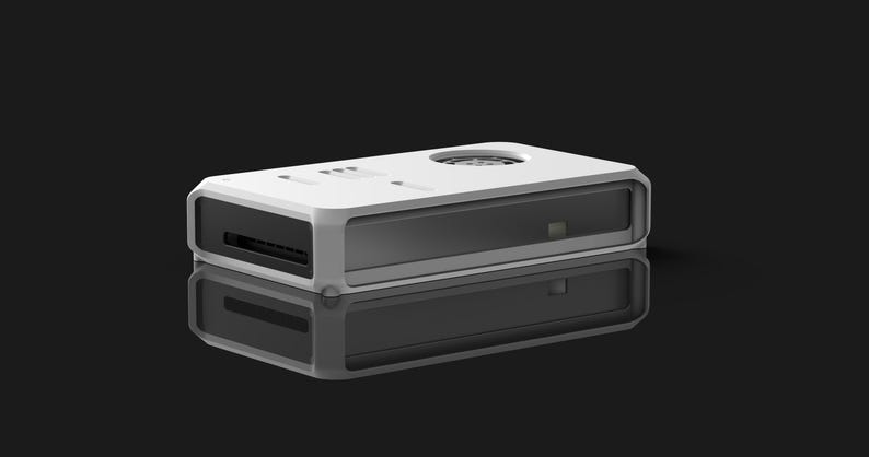 May include: A white and gray rectangular electronic device with a rounded frame. The device has a dark gray interior and a circular vent on top. The device is reflected on a black surface.