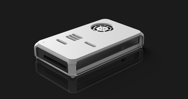 Op de afbeelding: Een wit rechthoekig elektronisch apparaat met een afgerond frame, ventilatieopeningen en een cirkelvormige ventilator aan de bovenkant. Het apparaat heeft een sleuf aan de voorkant en staat tegen een zwarte achtergrond. Het is waarschijnlijk een computercomponent of een vergelijkbaar technisch product.