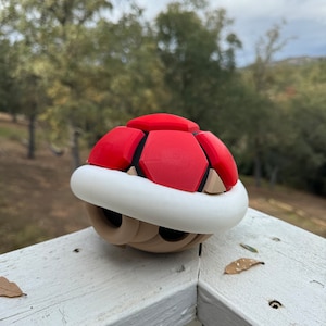 May include: A red and brown 3D printed shell with a white rim. The shell is shaped like a turtle shell and has a textured surface.