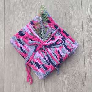 May include: A pink, blue, and gray crocheted blanket tied with a matching ribbon and decorated with a sprig of lavender.