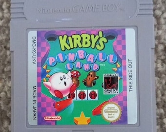 May include: A gray Nintendo Game Boy cartridge for Kirby's Pinball Land. The label features Kirby, a mushroom, and a brown creature. The game title is in a colorful design with a pink and teal background. The cartridge reads "Made in Japan."