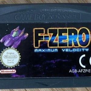 Può includere: Una cartuccia per Game Boy Advance per il gioco F-Zero: Maximum Velocity. La cartuccia è grigio scuro con un'etichetta con un'astronave viola e il titolo del gioco in blu e oro. Include il sigillo di qualità Nintendo.