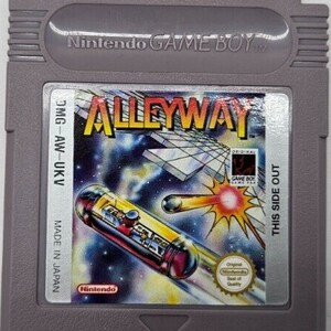 以下が含まれることがあります： 「Alleyway」のグレーの任天堂ゲームボーイカートリッジ。ラベルには、ゲームのタイトルが黄色とオレンジ色で表示され、宇宙をテーマにした背景と任天堂のロゴがあります。カートリッジには「Made in Japan」と記載されています。