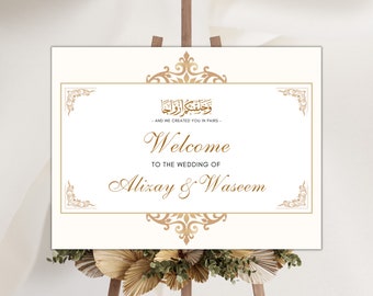 May include: A white wedding welcome sign with gold calligraphy and ornate borders. The sign reads "And We Created You In Pairs" in Arabic script, followed by "Welcome to the Wedding of Alizay & Waseem".