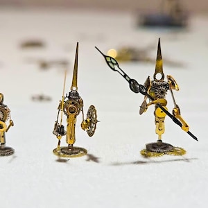 May include: Three steampunk sculptures made from watch components. The figures are predominantly gold-coloured, featuring intricate details and gear-like elements. Each figure has a unique design, with one resembling a bird.