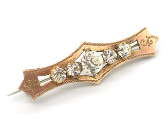 May include: A gold-toned brooch with a delicate design and five clear rhinestones.