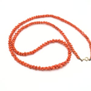 May include: A long necklace made of small, bright orange coral beads. The necklace is strung on a thin wire and has a gold clasp.