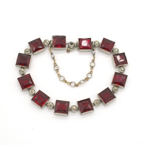 Könnte beinhalten: Ein rotes und silbernes Armband mit quadratischen roten Steinen und kleineren klaren Steinen. Das Armband hat einen Kettenverschluss.