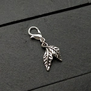 May include: Silver charm with a leaf design. The charm has a lobster clasp for attaching to a bracelet or necklace.