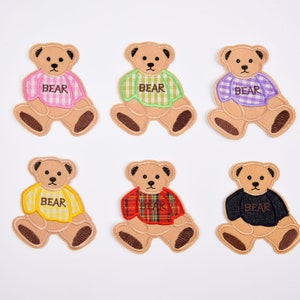May include: Six embroidered iron-on patches of brown teddy bears wearing different coloured plaid shirts. Each patch says "BEAR" on the shirt.