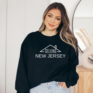 May include: Black sweatshirt with a white graphic design of a house with the text "SELLING NEW JERSEY".
