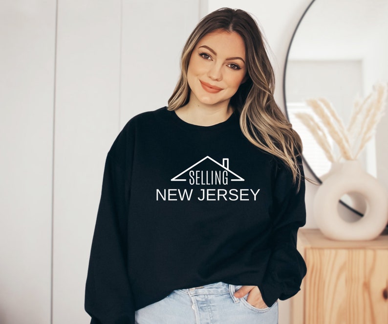 May include: Black sweatshirt with a white graphic design of a house with the text "SELLING NEW JERSEY".