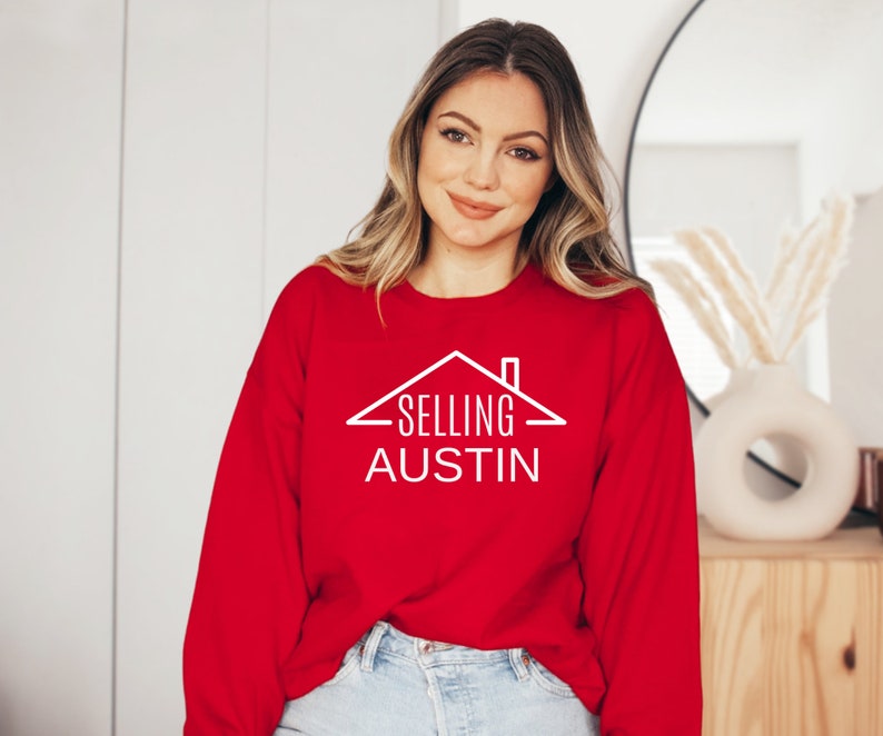 May include: A red sweatshirt with white text that reads "SELLING AUSTIN" and a house graphic above the text.