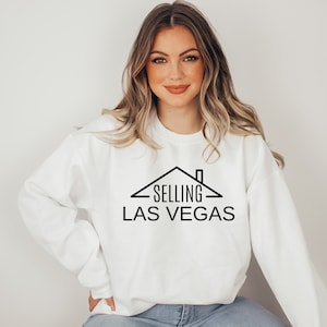 May include: White sweatshirt with black text that reads "SELLING LAS VEGAS" with a house graphic above the text.