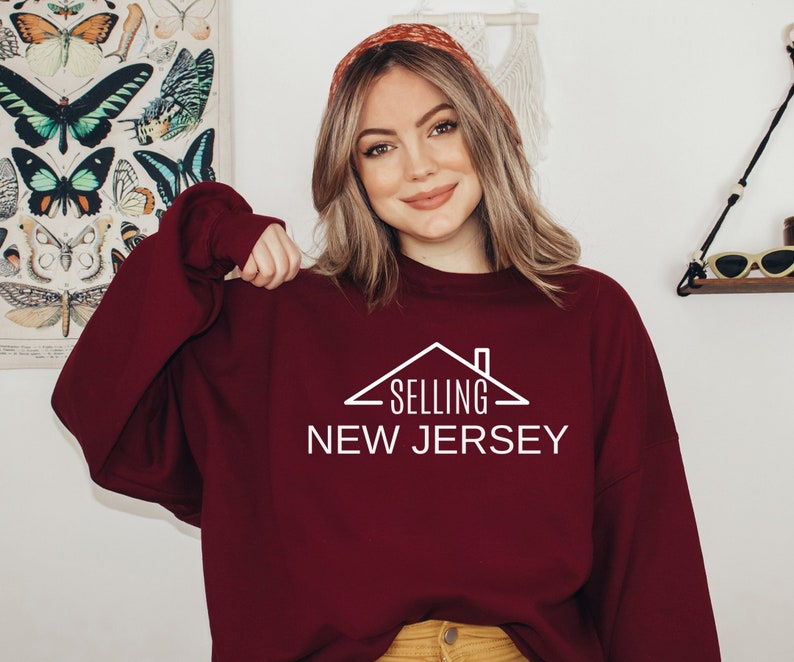 May include: A maroon sweatshirt with a white graphic of a house with the text "SELLING NEW JERSEY" on it.