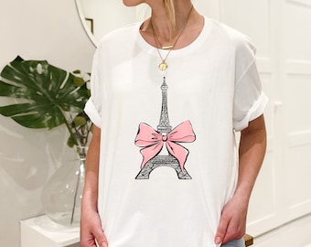 May include: White t-shirt with a black and white illustration of the Eiffel Tower with a pink bow on top.