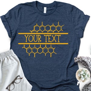 K&ouml;nnte beinhalten: Ein marineblaues T-Shirt mit einem Wabenmuster und dem Text "YOUR TEXT" in Gelb.