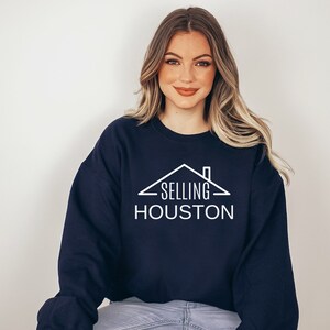 May include: A navy blue sweatshirt with a white graphic of a house with the text "SELLING HOUSTON" on it.