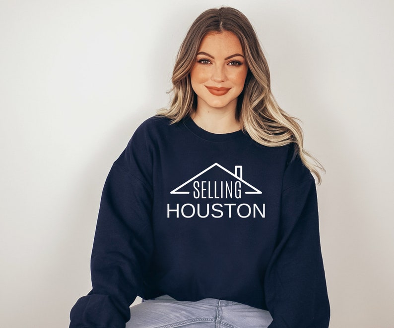 May include: A navy blue sweatshirt with a white graphic of a house with the text "SELLING HOUSTON" on it.