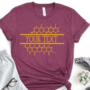 K&ouml;nnte beinhalten: Ein maroonfarbenes T-Shirt mit einem Wabenmuster und dem Text "YOUR TEXT" in Gelb.