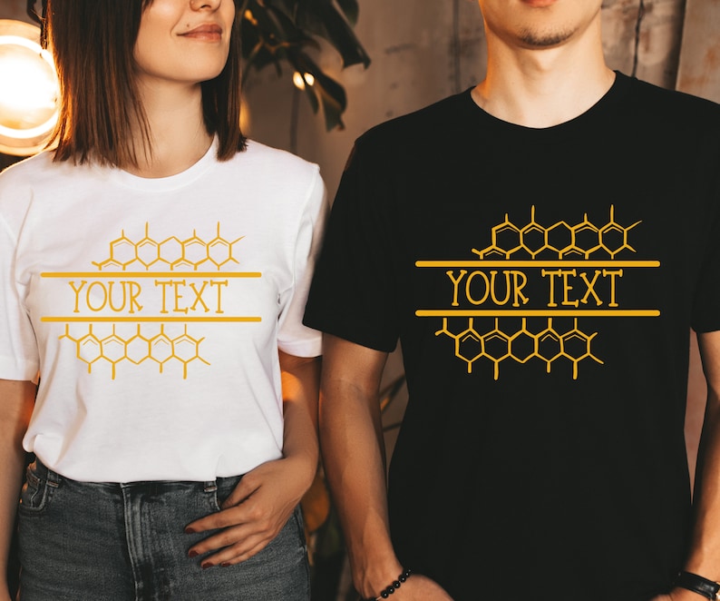 K&ouml;nnte beinhalten: Zwei T-Shirts mit einem Wabenmuster und dem Text "YOUR TEXT" darauf gedruckt. Das T-Shirt links ist wei&szlig; und das T-Shirt rechts ist schwarz.