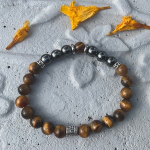 May include: A brown and black tiger's eye beaded bracelet with silver accents. The bracelet has a silver bead with a geometric design.