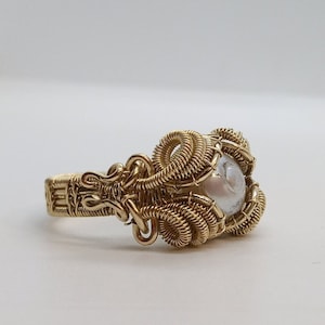 May include: A gold wire wrapped ring featuring a white pearl-like stone in the centre.