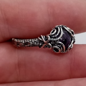 Puede incluir: Un anillo de alambre plateado con una piedra preciosa de amatista púrpura.