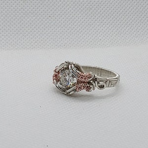 May include: A silver and copper wire wrapped ring with a clear gemstone in the centre.