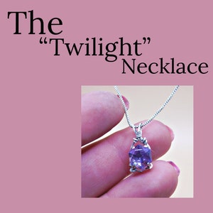 Puede incluir: Un collar de cadena de plata con un colgante de piedra preciosa púrpura. El colgante está envuelto en alambre y tiene una forma de lágrima facetada. El collar se llama "The Twilight" Necklace.