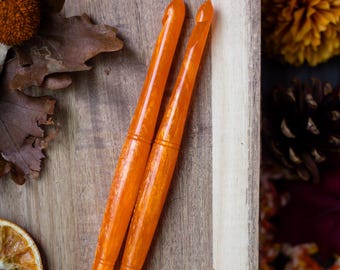 May include: Two translucent orange crochet hooks with a marbled texture. Each hook features a pointed tip, a deep throat for yarn, and a smooth, tapered shaft with two horizontal decorative grooves near the center of the handle.