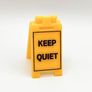 May include: A yellow plastic sign with black text that reads "KEEP QUIET".