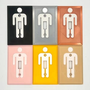 K&ouml;nnte beinhalten: Sechs Lichtschalterabdeckungen in verschiedenen Farben: Schwarz, Silber, Kupfer, Rosa, Gelb und Beige. Jede Abdeckung zeigt eine wei&szlig;e Silhouette einer Person mit einem Lichtschalter in der Mitte.