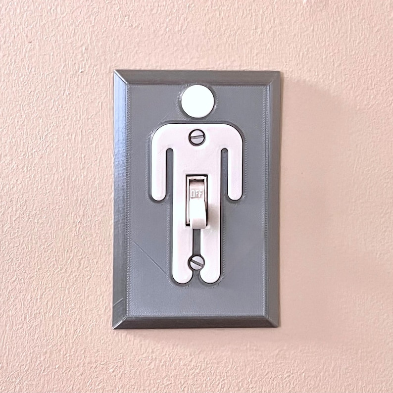 K&ouml;nnte beinhalten: Ein grauer Lichtschalter mit einer wei&szlig;en Silhouette einer Person mit einem Lichtschalter in der Mitte des K&ouml;rpers. Der Schalter ist in der Aus-Position.