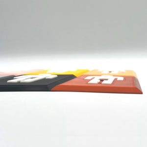 K&ouml;nnte beinhalten: Ein Satz von f&uuml;nf bunten rechteckigen Fliesen mit einer wei&szlig;en Figur auf jeder Fliese. Die Fliesen sind in einer Reihe angeordnet, wobei die orange Fliese vorne und die schwarze Fliese hinten ist. Die Fliesen sind aus glattem, hartem Kunststoff.