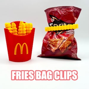 May include: A red container shaped like a fast-food fry box with yellow fries and a yellow "M" logo. Next to it is a bag of chips secured with a yellow bag clip. The text "FRIES BAG CLIPS" is at the bottom.