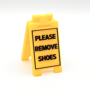 May include: Yellow sign with black text that reads "PLEASE REMOVE SHOES".