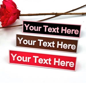 Può includere: Tre etichette rettangolari con testo bianco che dice "Your Text Here". L'etichetta superiore è nera con bordo rosa, l'etichetta centrale è marrone con bordo bianco e l'etichetta inferiore è rossa con bordo bianco.