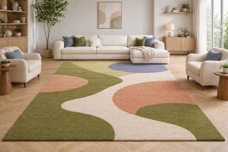 K&ouml;nnte beinhalten: Ein gro&szlig;er Teppich mit abstraktem Design in Gr&uuml;n-, Pfirsich-, Blau- und Cremet&ouml;nen. Der Teppich befindet sich in einem Wohnzimmer mit einem wei&szlig;en Sofa und Sesseln. Die Abmessungen des Teppichs sind nicht sichtbar.