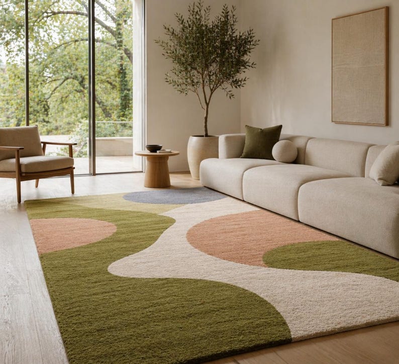 K&ouml;nnte beinhalten: Ein gro&szlig;er, rechteckiger Teppich mit einem abstrakten Design. Der Teppich hat ein wellenf&ouml;rmiges Muster mit gr&uuml;nen, pfirsichfarbenen, grauen und cremefarbenen Abschnitten. Der Teppich liegt auf einem Holzboden in einem Wohnzimmer.