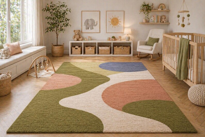 K&ouml;nnte beinhalten: Ein farbenfroher Teppich mit abstraktem Design in Gr&uuml;n-, Pfirsich-, Blau- und Cremet&ouml;nen. Der Teppich befindet sich in einem Kinderzimmer, mit einem Kinderbett, einem Schaukelstuhl und dekorativen Elementen.