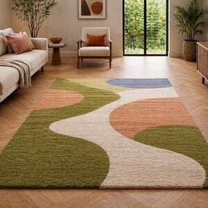 K&ouml;nnte beinhalten: Ein rechteckiger Teppich mit einem abstrakten Design in Gr&uuml;n, Pfirsich, Blau und Creme. Der Teppich hat ein wellenf&ouml;rmiges Muster und liegt auf einem Holzboden, was dem Wohnzimmer eine moderne Note verleiht. Ungef&auml;hre Abmessungen: 200 cm x 300 cm.