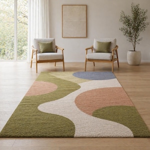 K&ouml;nnte beinhalten: Rechteckiger Teppich mit abstraktem Design in Gr&uuml;n, Rosa, Blau und Creme. Der Teppich hat ein wellenf&ouml;rmiges Muster und liegt auf einem Holzboden. Im Hintergrund befinden sich zwei Sessel mit olivgr&uuml;nen Kissen.